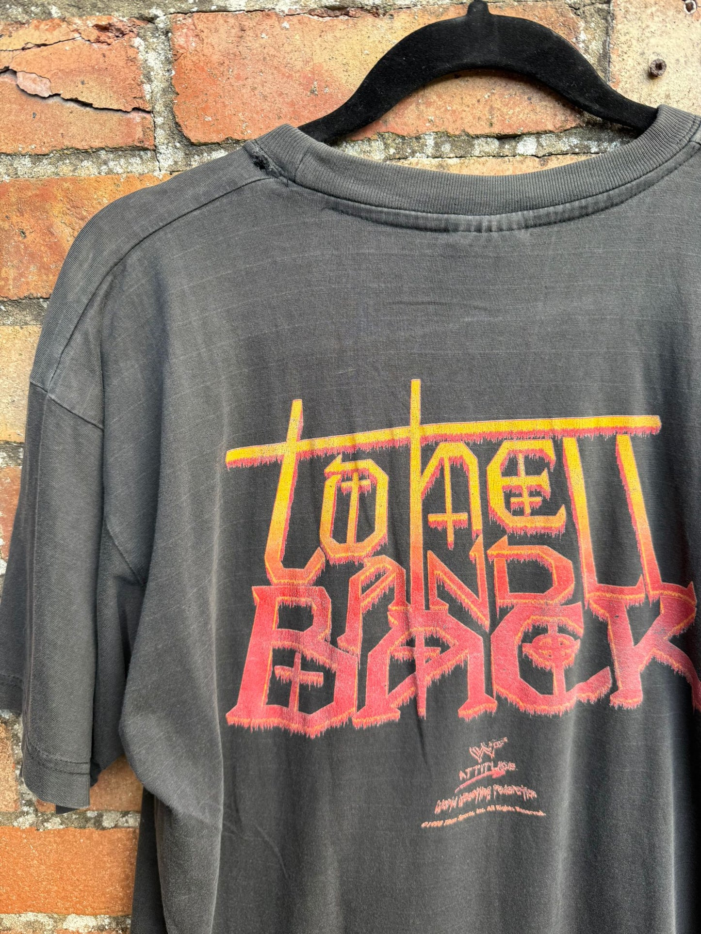 Black t-shirt with text to hell and back, on a hanger against a brick wall