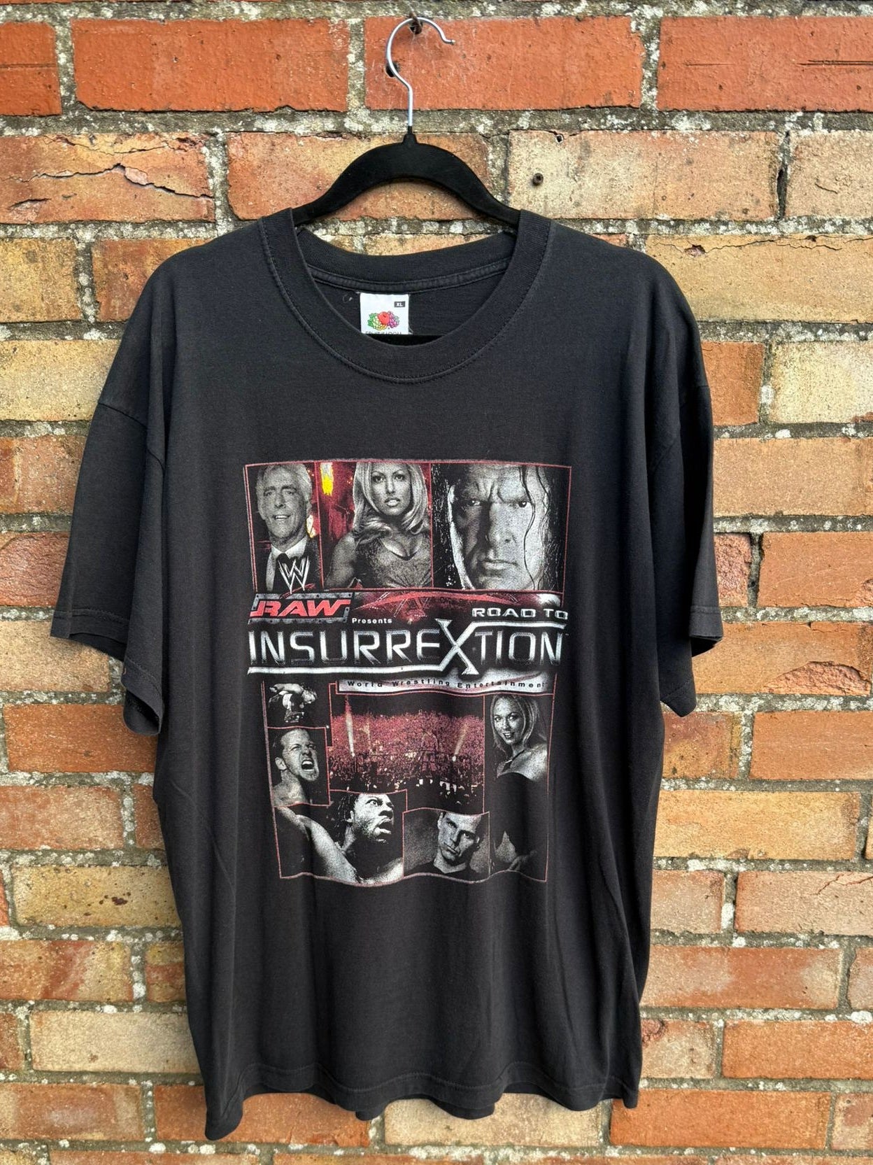 Black t-shirt with text RAW Road to Insurrextion and graphic design with wrestlers, hanging against a brick background