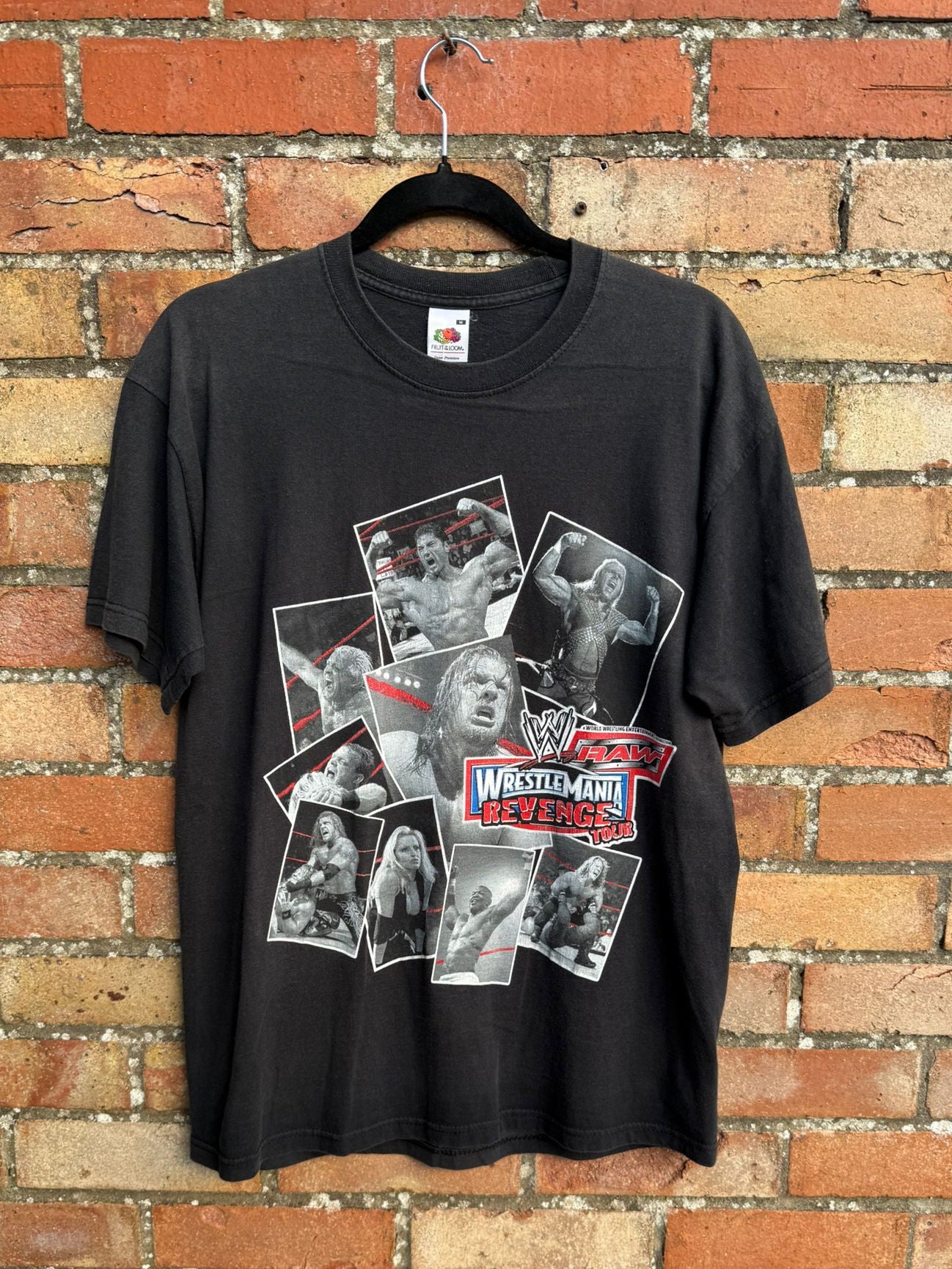Black t-shirt with Wrestlemania wrestling graphic on a hanger against a brick wall
