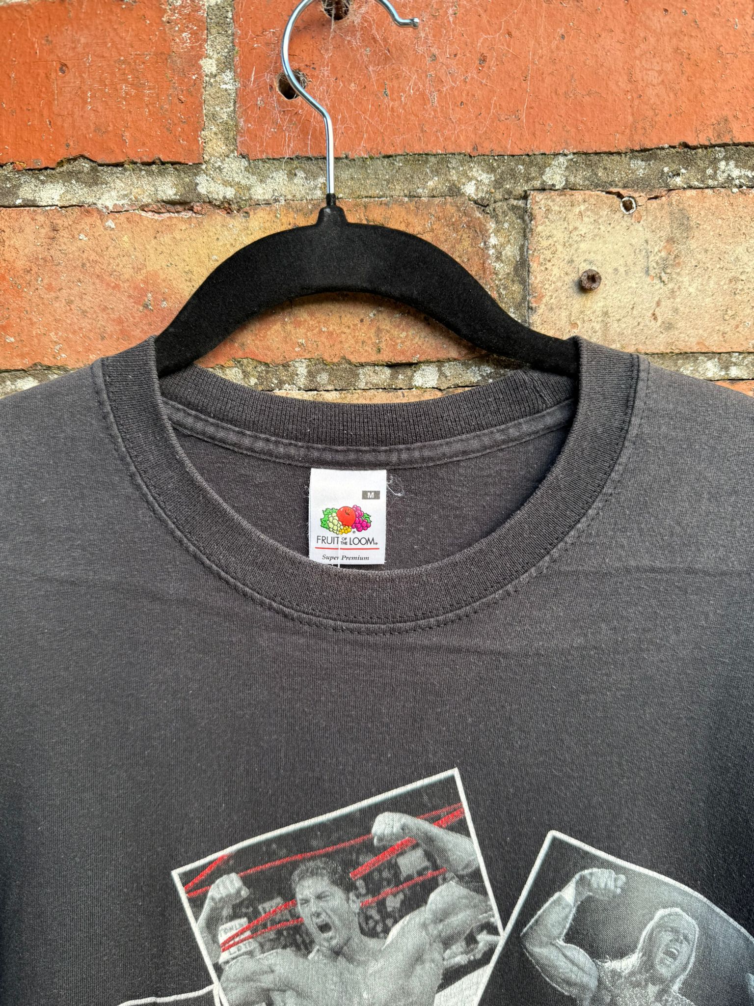 Black t-shirt with graphic designs on a Fruit of the Loom tag, hanging against a brick wall.