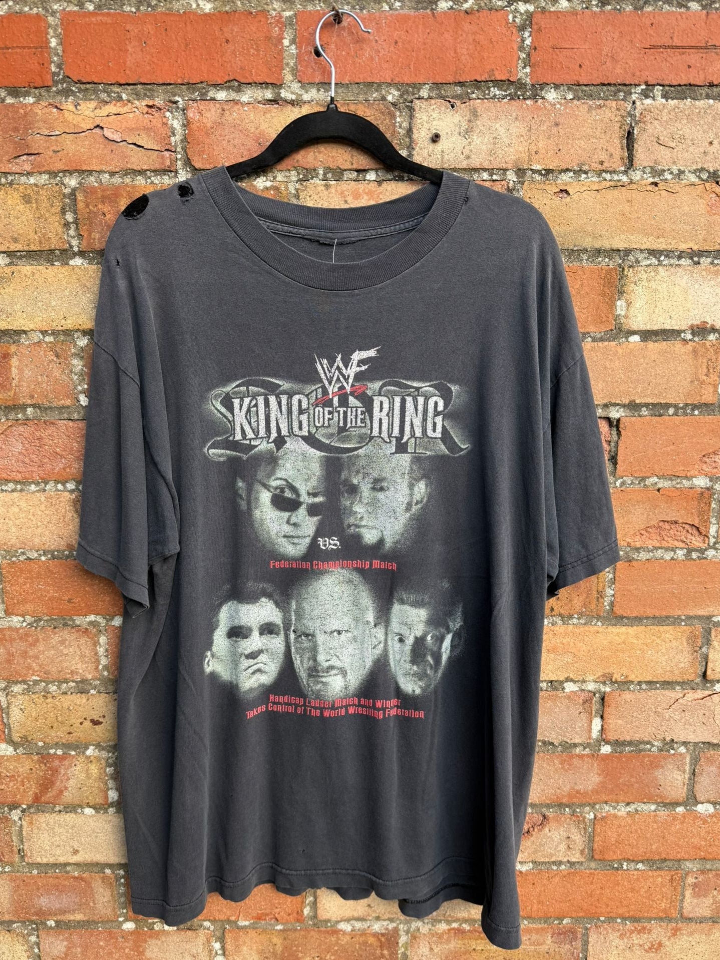 Black t-shirt with King of the Ring graphic design on a hanger against a brick wall