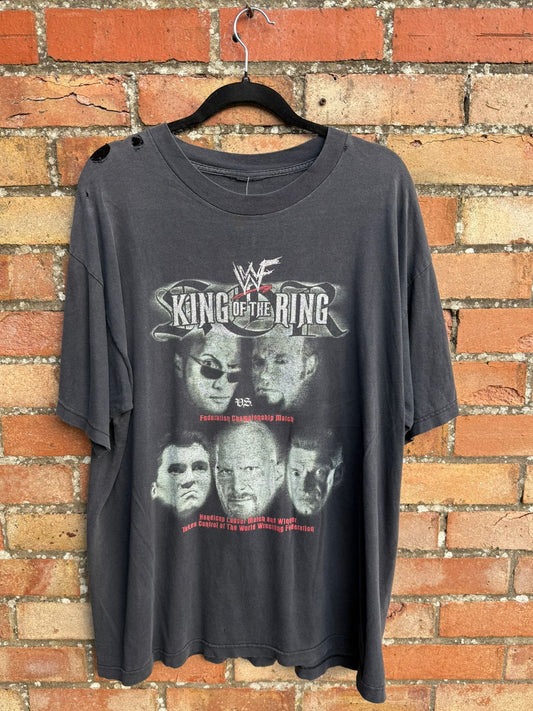 Black t-shirt with King of the Ring graphic design on a hanger against a brick wall