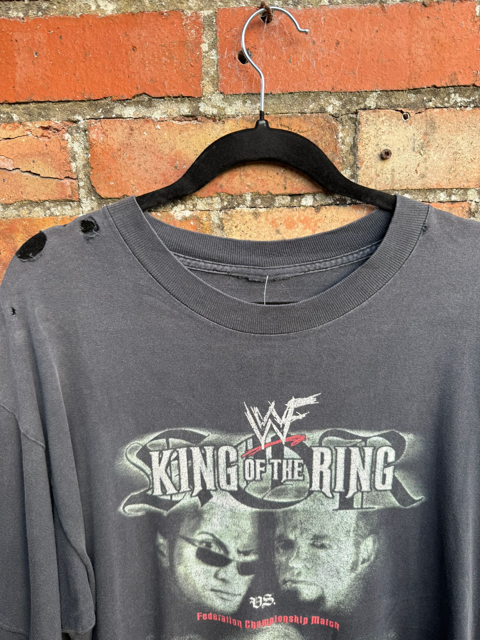 Close-up of top of t-shirt showing cut tag and holes in one shoulder, with King of the Ring text