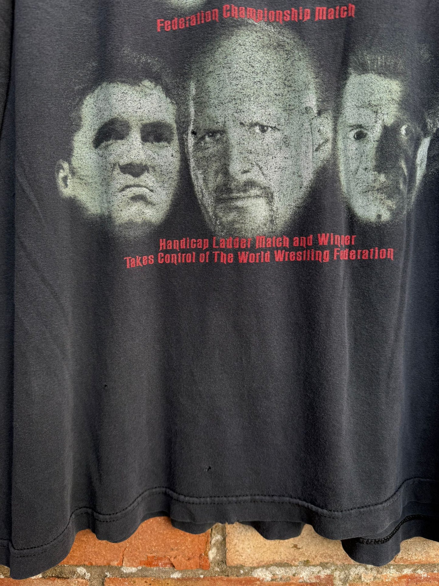 Black t-shirt with graphic of three faces and text on a brick surface