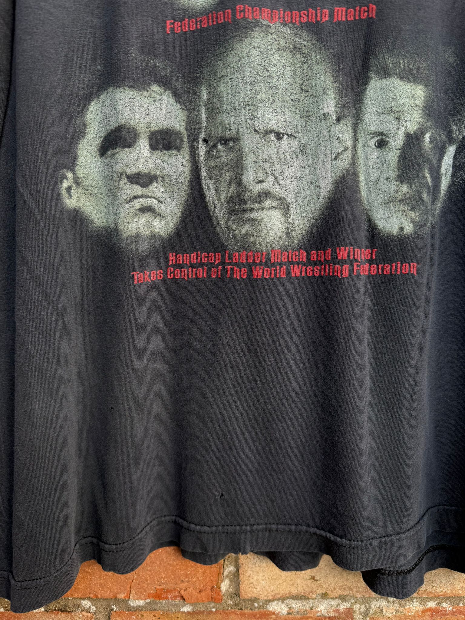 Black t-shirt with graphic of three faces and text on a brick surface