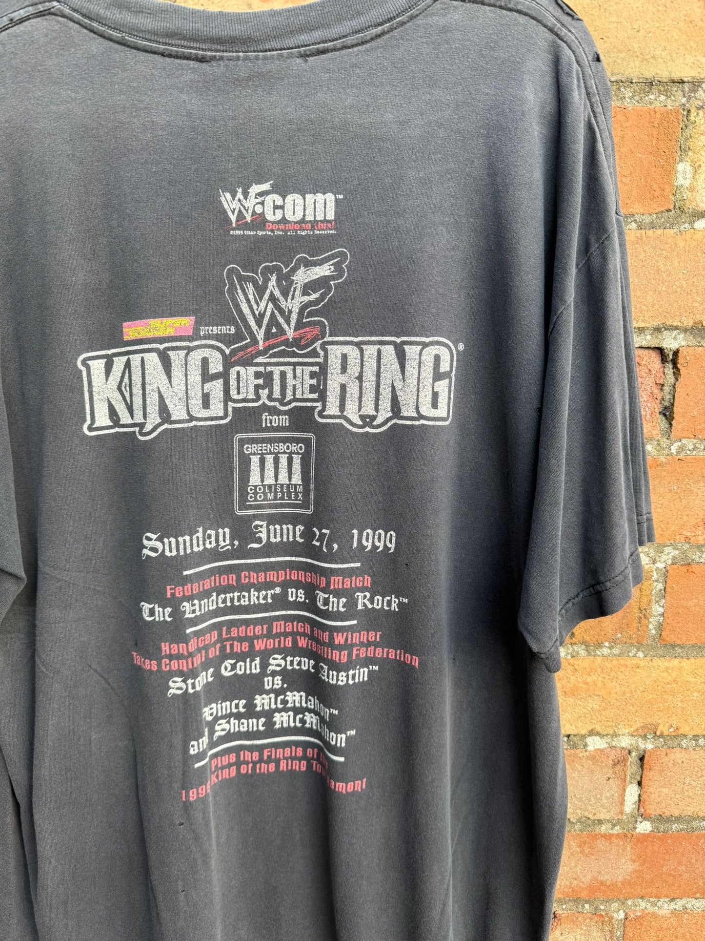 Faded black t-shirt with 'King of the Ring' wrestling event graphic against a brick wall.