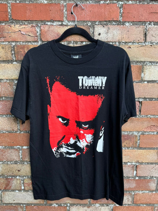 Black t-shirt with red and white Tommy Dreamer graphic design on a hanger against a brick wall.