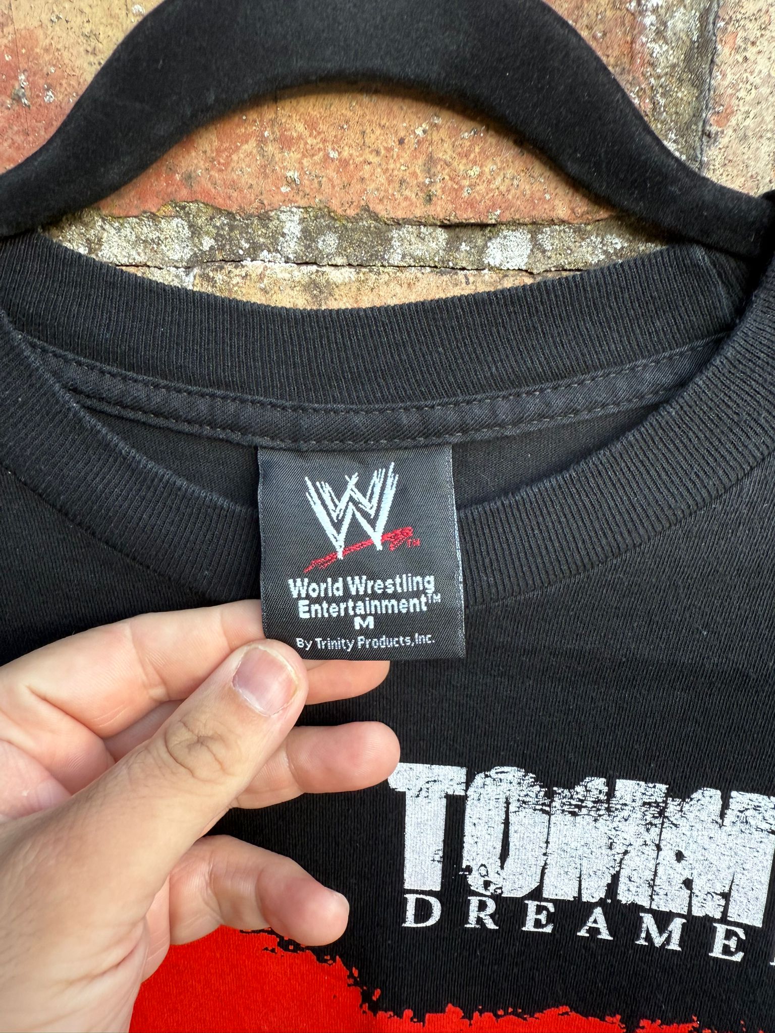 Black t-shirt with WWE logo tag and 'Tommy Dreame' text on a textured surface.