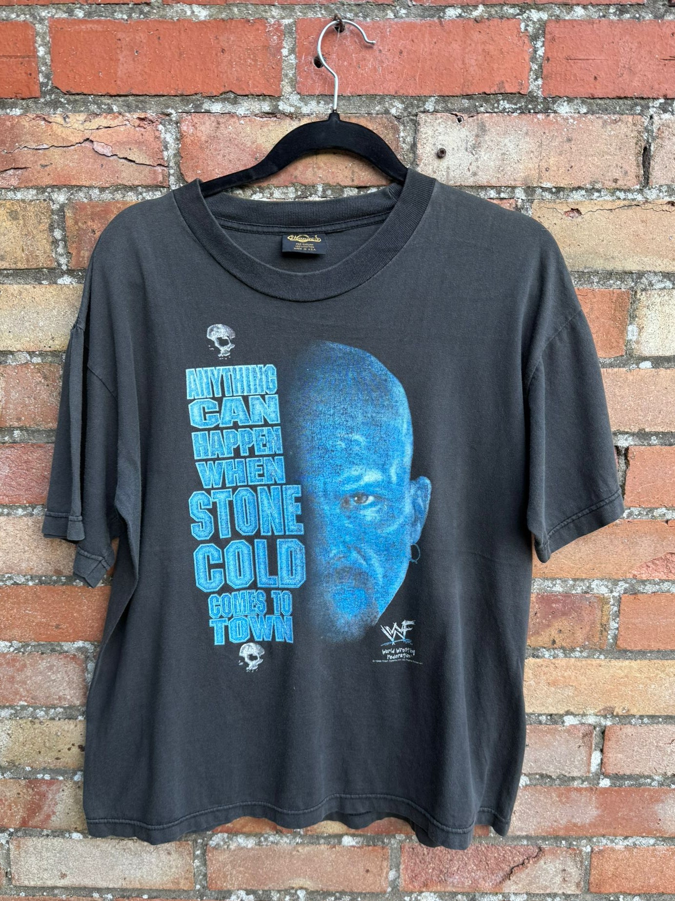 Black t-shirt with Stone Cold graphic and Anything Can Happen text hanging against a brick wall background