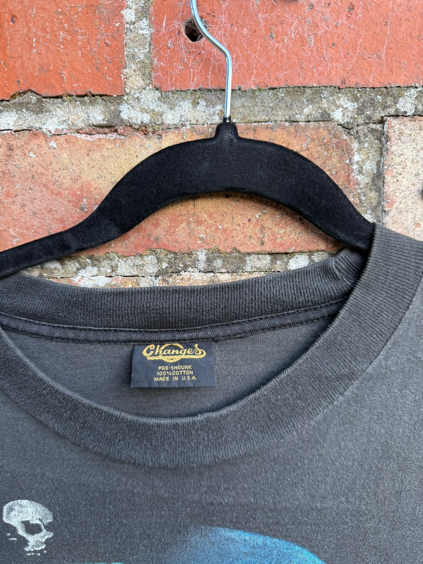 Black t-shirt with close-up of a Changes brand label on a hanger against a brick wall.