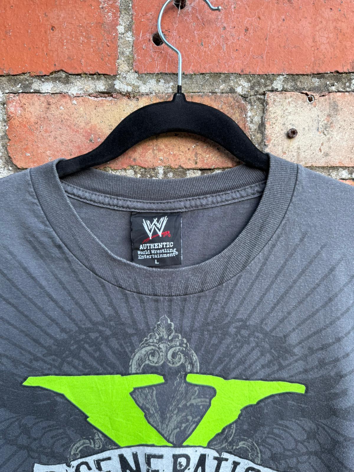 Gray t-shirt with green logo and WWE tag on a hanger against a brick wall.