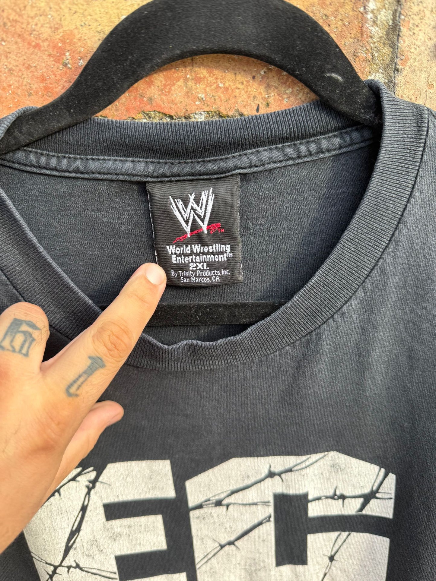 Black t-shirt with WWE logo and text, held by a hand.