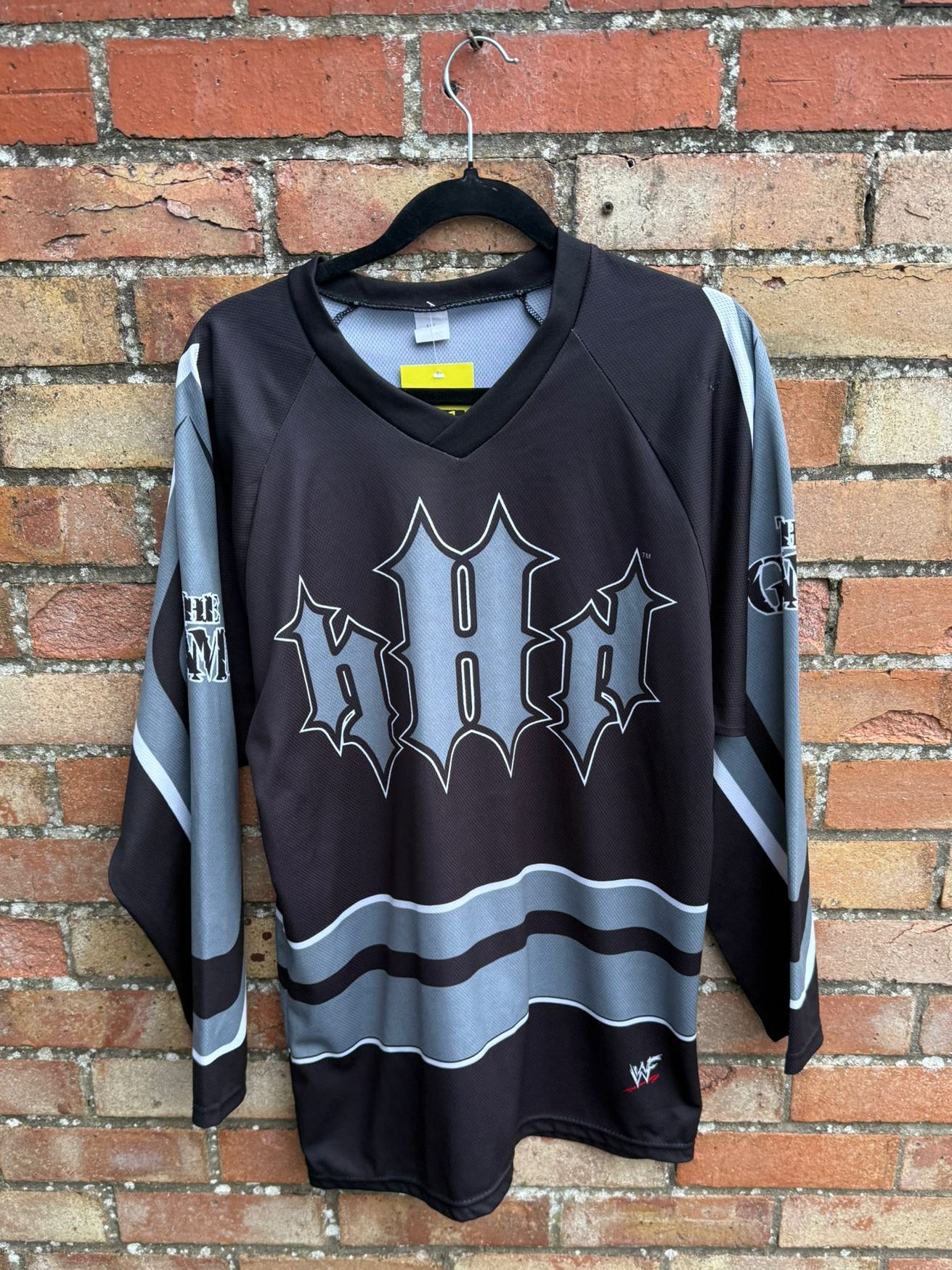 Black sports jersey with WWF Triple H logo on a hanger against a brick wall