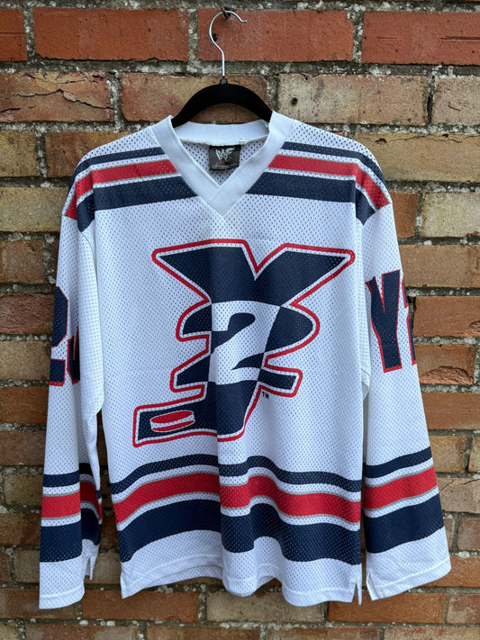 White hockey jersey with Y2J red and blue accents hanging against a brick wall.