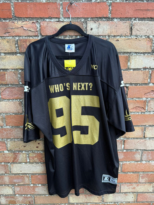 Black sports jersey with 'WHO'S NEXT?' and number '95' on a brick wall background