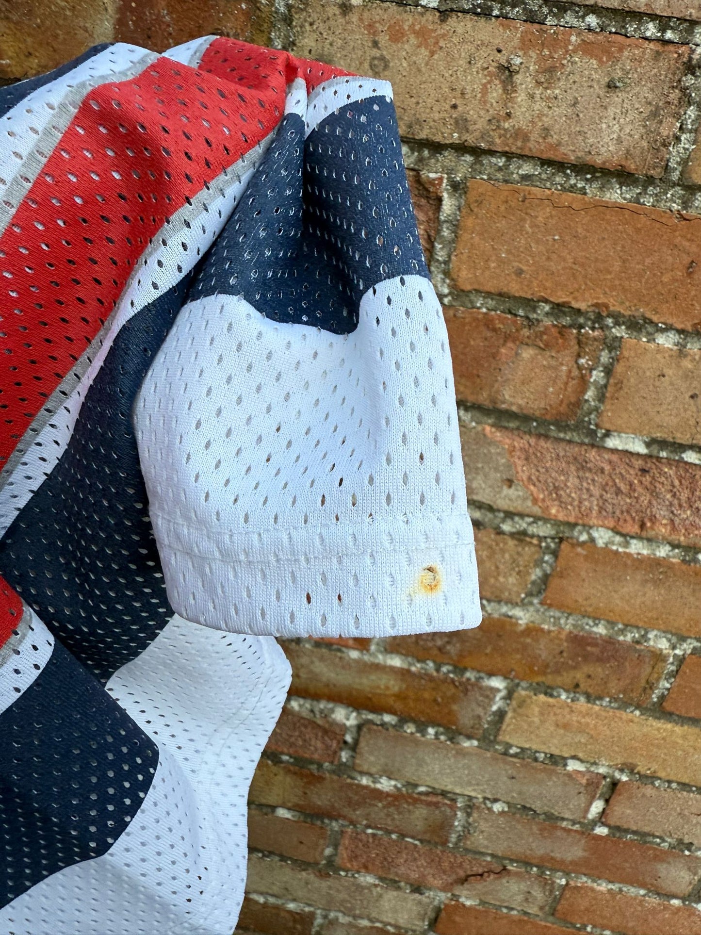 Textured fabric with red, white, and blue pattern highlighting a small possible burn hole on the sleeve end