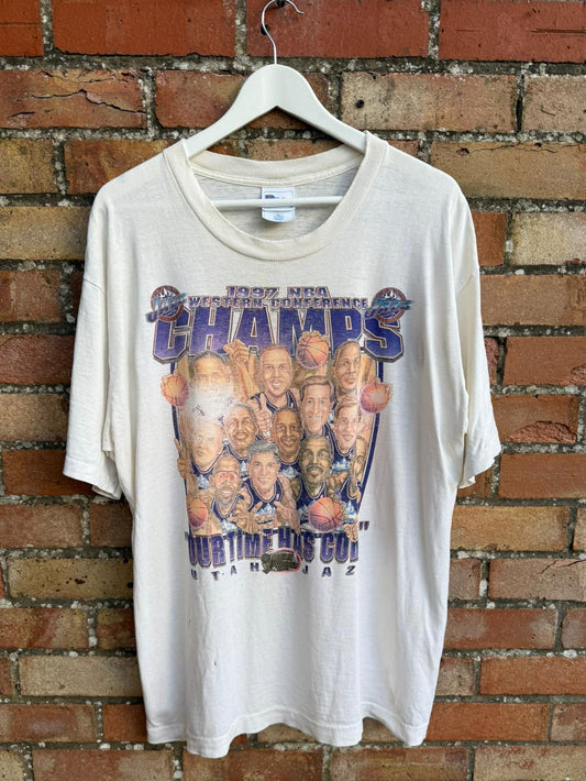 White t-shirt with Utah Jazz sports team graphic and 'Western Conference Champs' text on a brick wall background